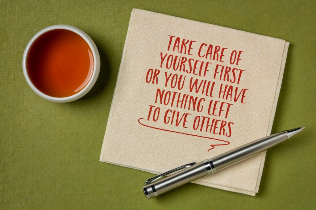 A napkin with a pen and a cup of tea with a note on the napkin saying take care of yourself first or you will have nothing left to give others.