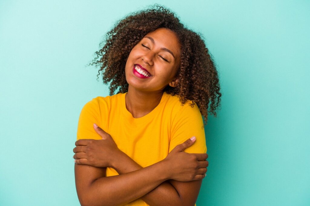 Young african american woman with curly hair isolated on blue background laughing and having fun.