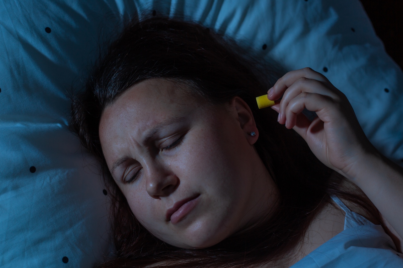 A woman lying in bed holding a yellow earplug.