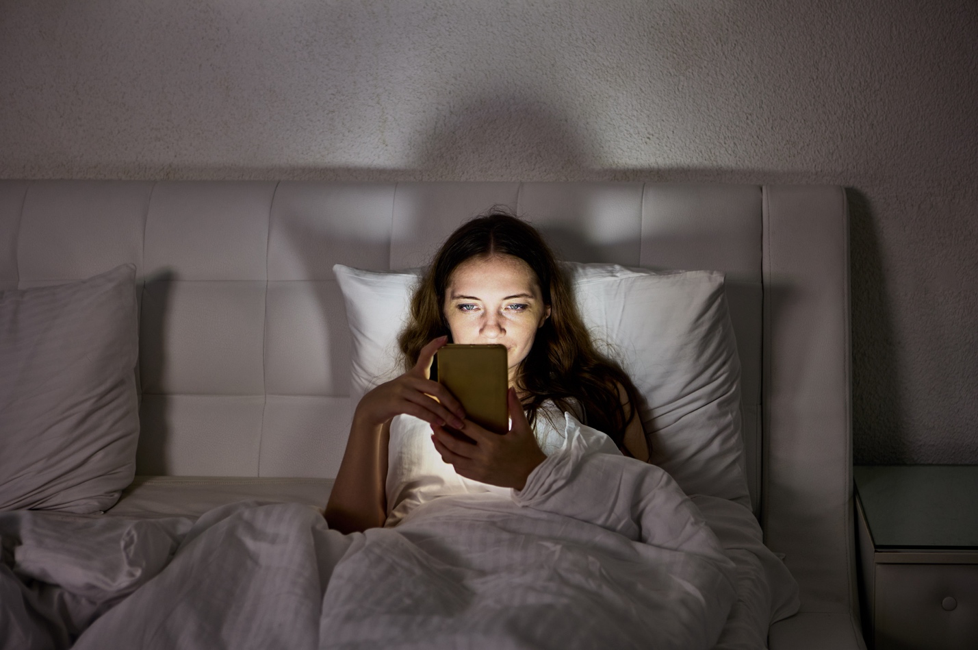 A woman lying in bed looking at her phone.