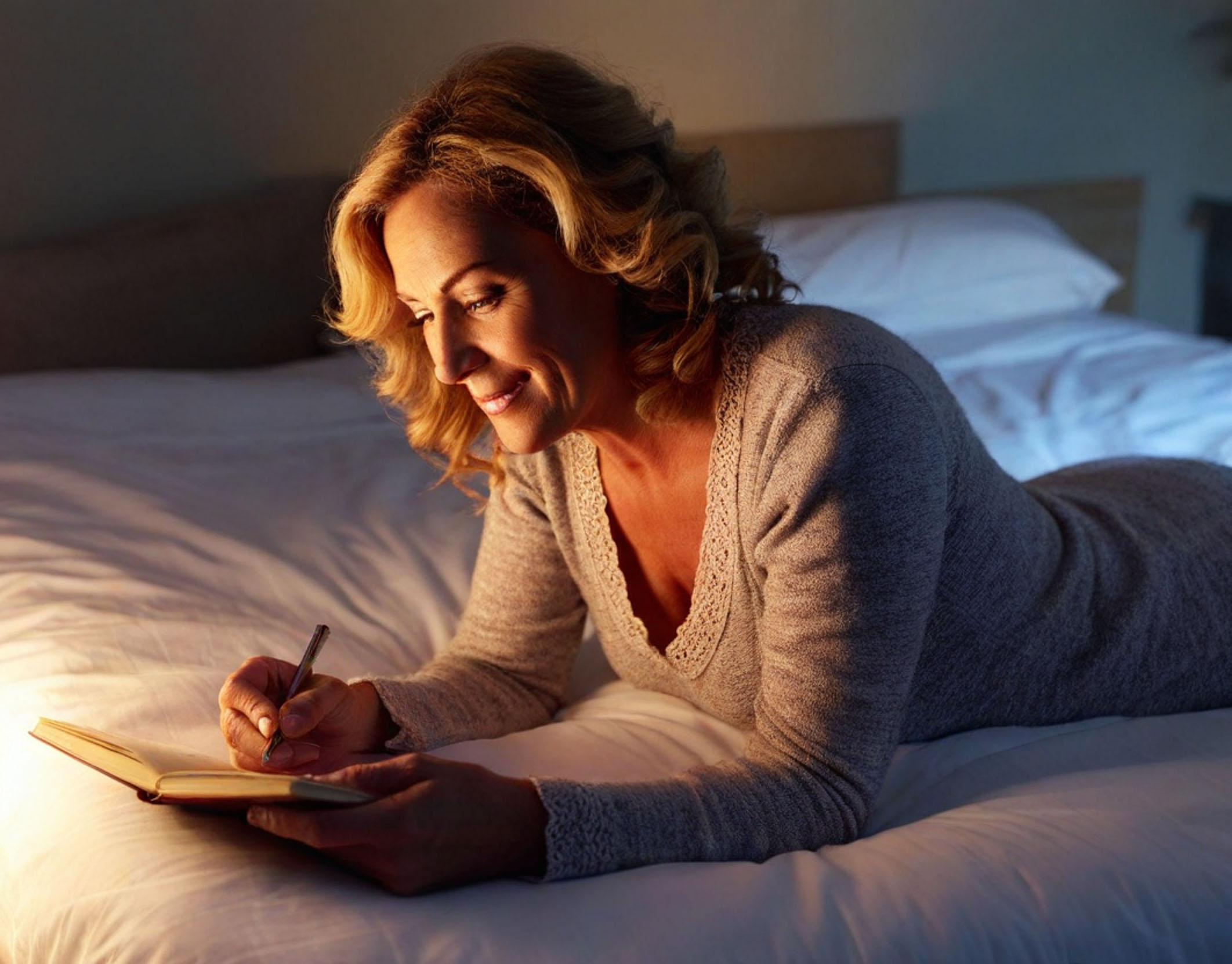 A person lying on a bed writing in journal.